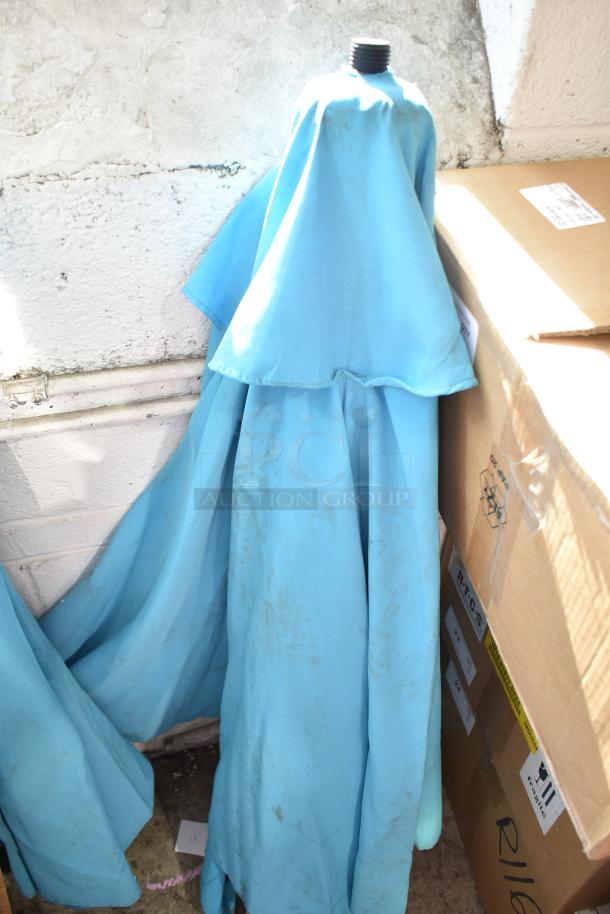 Two blue patio umbrellas, slightly worn condition, bundled together, metal pole visible at the top, resting against boxes.