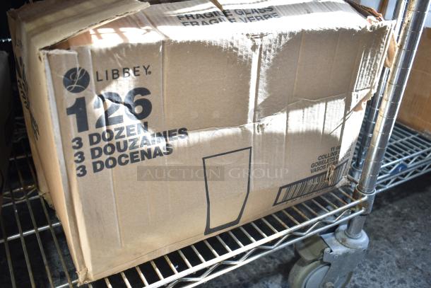 Damaged box with Libbey 126 Heavy Base 11 oz. Collins glasses, labeled "3 dozen," on a metal shelf.