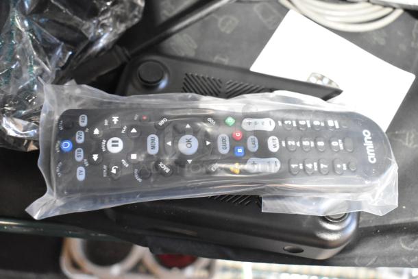Remote control wrapped in plastic with "Amino" branding, part of a lot including a power conditioner and barcode scanner.