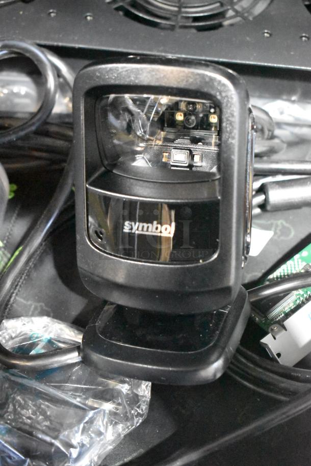 Symbol barcode scanner, black, shown on a table with cables. Part of a lot including a power conditioner and remote.