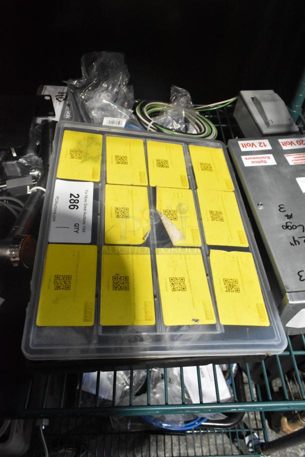 Closed toolbox with yellow-labeled compartments, various small parts inside, shelf includes cables and electronic boxes.