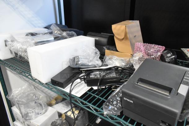 Assorted tech items including Epson M244A receipt printer, Symbol barcode scanner, remote, card reader on metal shelf.