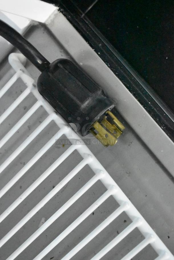 Close-up of power plug for True GDM-49F-HC freezer. Shows three-prong plug and nearby metal shelving.