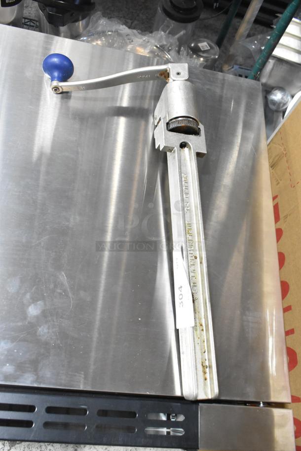 Edlund commercial can opener with blue handle, metal body, marked "Edlund Co. Burlington VT USA." Mounted on stainless steel surface.