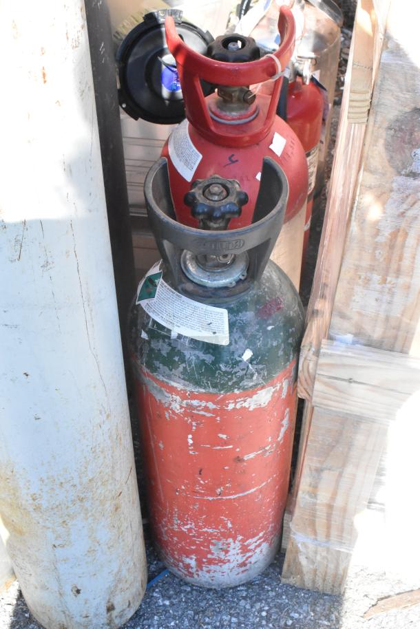 Rustic gas tanks, visibly worn, with attached valves and labels. Auction includes 7 tanks; local pickup required.