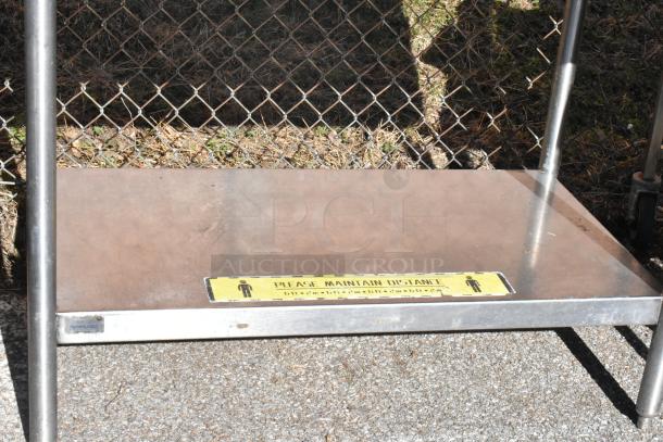 2 commercial tables with under shelf; one has commercial casters. Metal construction, visible "Please Maintain Distance" sign.