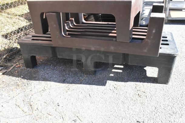 Three poly dunnage racks, two brown and one black, stacked on asphalt. Durable, ideal for storage.