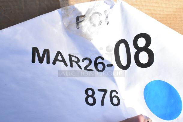 Package label with "MAR26-08" and "876" in bold black text against a white background, partially obscured by tape and a blue dot.