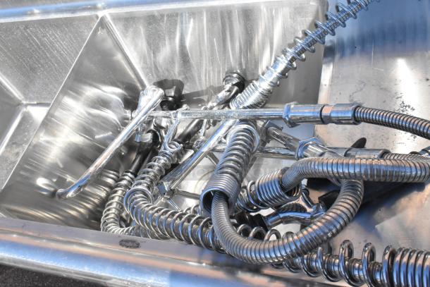 Commercial 3 bay sink with dual drain boards, stainless steel, featuring coiled hoses and faucets. Appears in good condition.