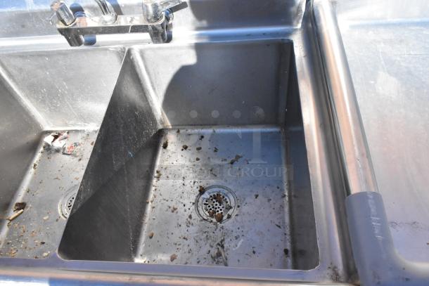Commercial 2-bay sink with left side drain boards, showing signs of use with residue and debris present.