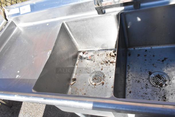 Commercial 2 bay sink with left side drain boards, stainless steel, visible wear, needs cleaning, auction number 332 displayed.