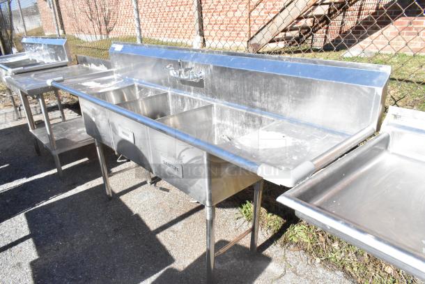 Commercial 3-bay sink with dual drain boards and faucet; stainless steel, labeled rinse and sanitize, outdoor setup.