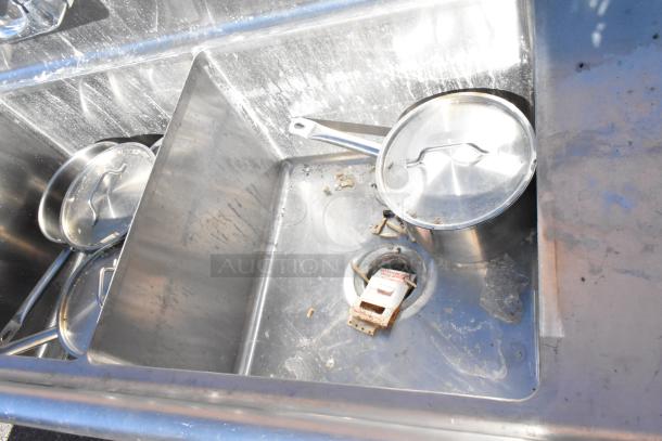 Commercial 3 bay stainless steel sink with dual drain boards, containing pots and debris. Good working condition.