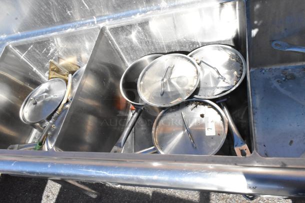 Commercial 3 bay sink with dual drain boards, showing used condition with pots and debris inside.