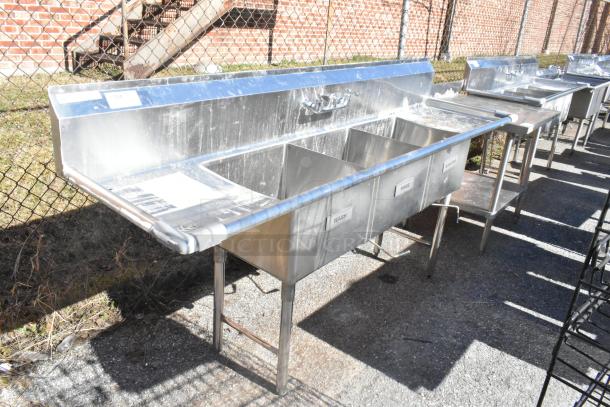 Commercial 3 bay sink with dual drain boards, stainless steel, labelled "Wash," "Rinse," "Sanitize," used condition, outdoors.