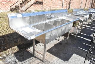 Commercial 3 bay sink with dual drain boards, stainless steel, labelled "Wash," "Rinse," "Sanitize," used condition, outdoors.