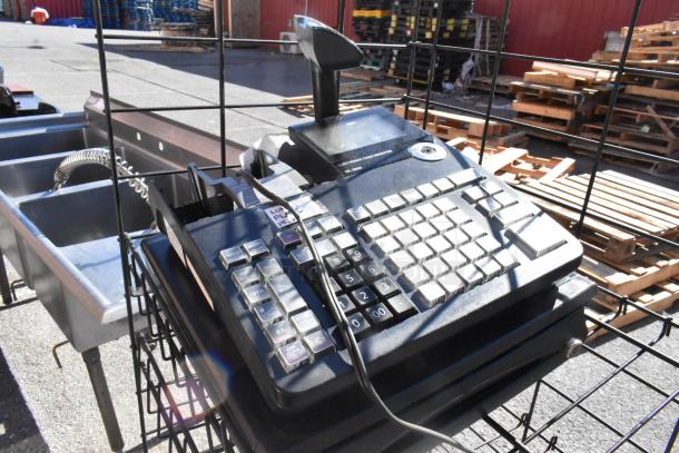 Black finish merchandising rack with cash register; condition appears used, includes keypad and scanner. Buyer must dismantle.