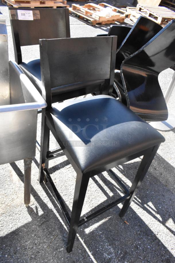 Black bar height chair with cushioned seat, wooden frame, slight wear visible. Part of a set of 14 chairs and 4 tables.