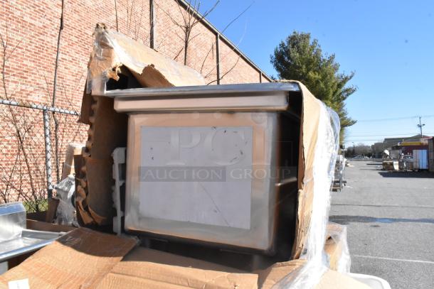 Brand new stainless steel sink with minor scratches and dents, partially wrapped in damaged cardboard packaging.