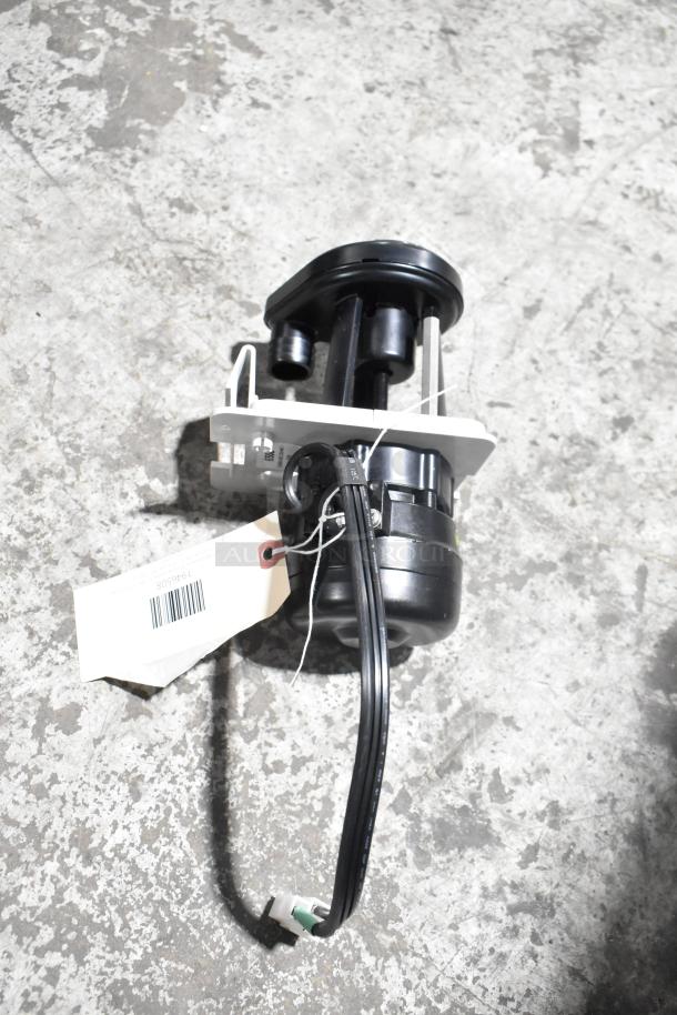 Black mechanical component labeled "Brand New Scratch and Dent" with attached barcode tag on concrete surface.