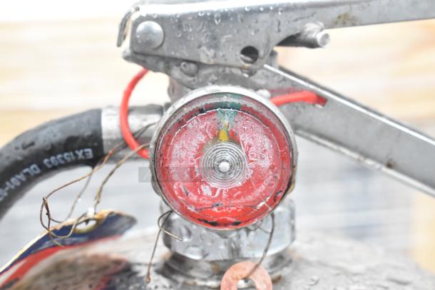 Close-up of a metal fire extinguisher gauge, showing red pressure indicator and attached hose with visible label. Condition appears used.