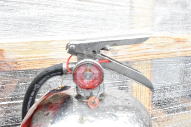 Two fire extinguishers with metal handles and red pressure gauges, slightly wet. Buyer must pick up; no shipping available.