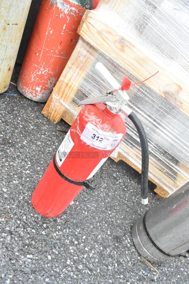Red fire extinguisher with hose and handle, showing wear. Label states auction info and item number 372. Buyer pickup only.