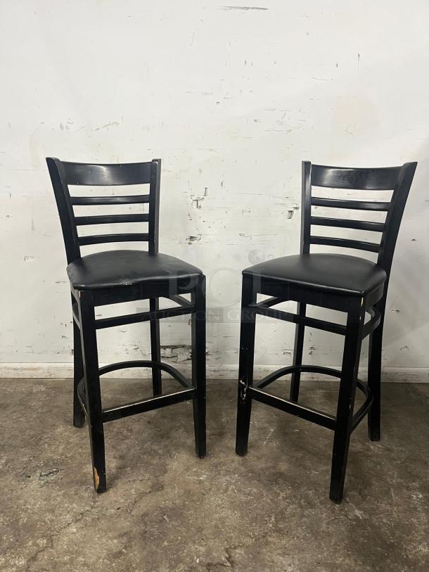 Black sandthru finish bar stools with faux leather seats, ladder-back design, visible wear on legs.