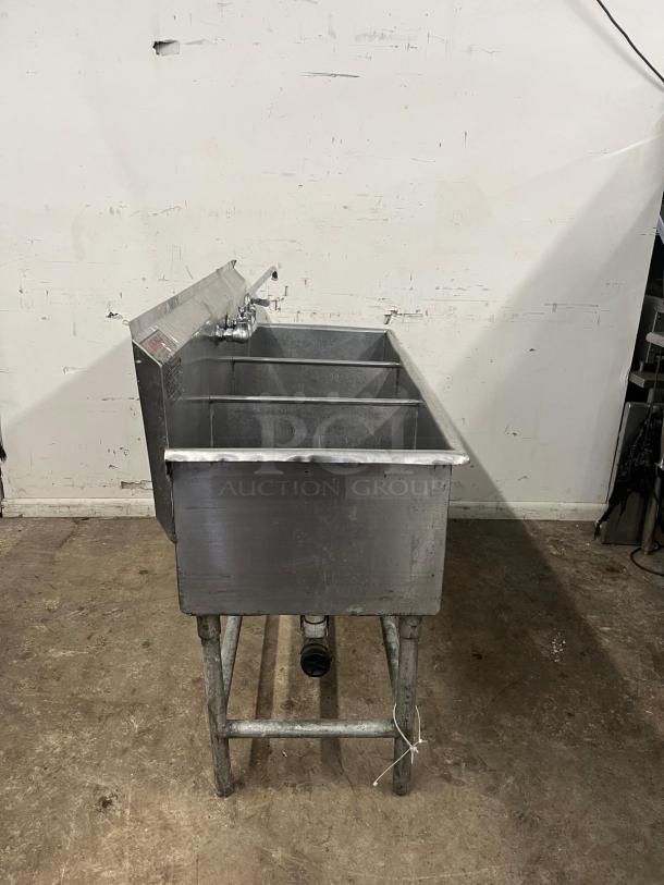 Stainless steel 3 compartment sink with attached faucet and sturdy metal legs, showing signs of wear.