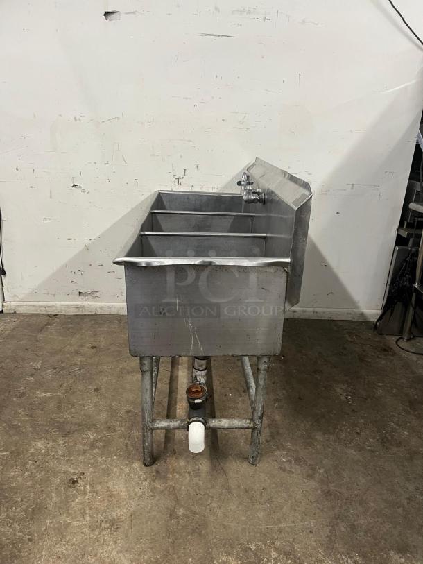 Industrial 3-compartment sink with faucets, stainless steel, worn condition, suitable for commercial use, visible plumbing.
