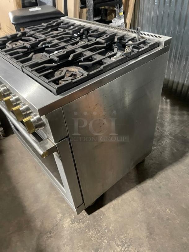 Monogram stainless steel gas-powered 6-burner range/oven combo with wired oven rack, on legs, showing some surface wear.