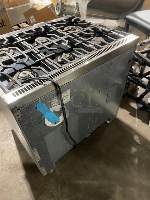 Monogram stainless steel gas-powered 6-burner range/oven combo with wired oven rack, on legs, shown from side view.