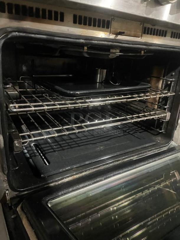 Stainless steel Monogram 6-burner range/oven combo with wired oven rack, gas-powered, on legs, interior view shown.