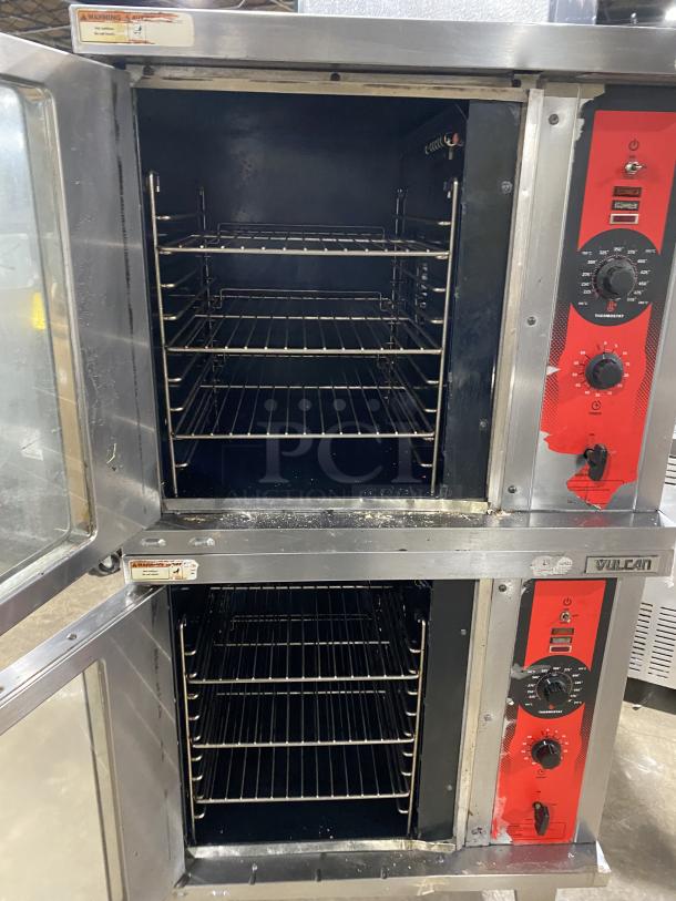 Vulcan stainless steel gas-powered double-stacked convection oven with wired racks, on legs. Visible controls and warning label.