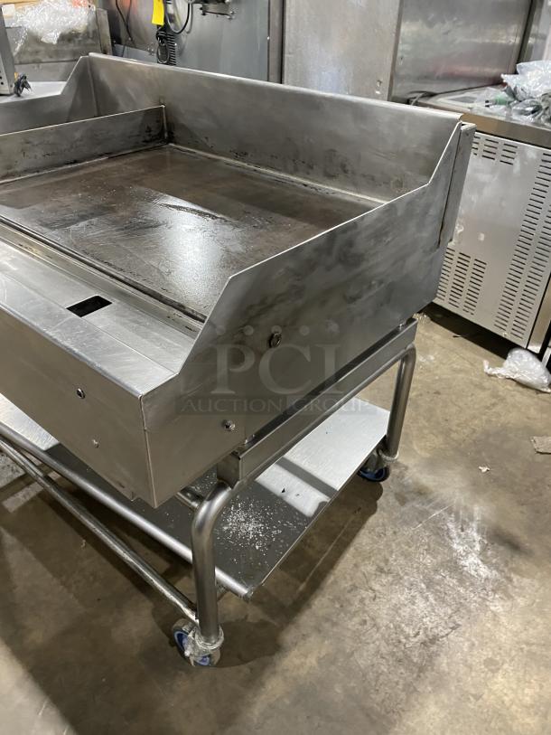 WoodStone stainless steel natural gas countertop plancha flat griddle with back and side splash, on welded stand with casters.