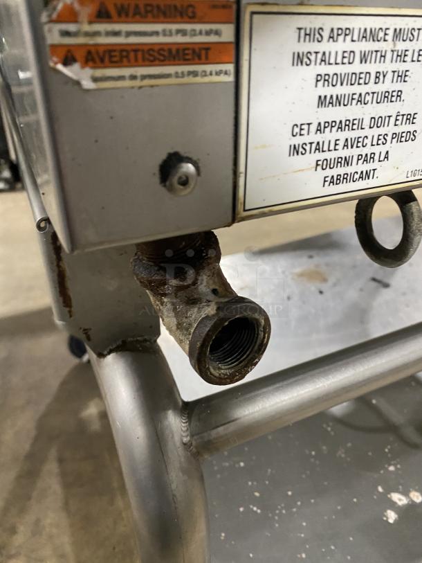 WoodStone stainless steel natural gas flat griddle with back and side splash, mounted on a welded stand with casters. Warning label visible.