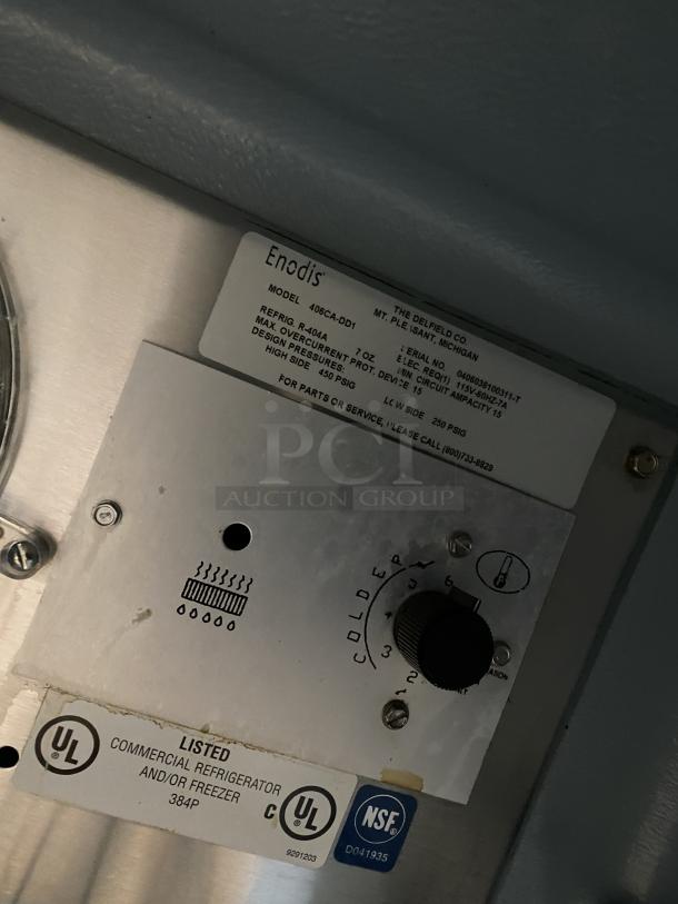 Delfield stainless steel undercounter refrigerator, model 406CA-DD1, with poly coated wire racks. Includes labels showing model, serial number, and certifications. In good condition, mounted on casters for mobility. 115V power.