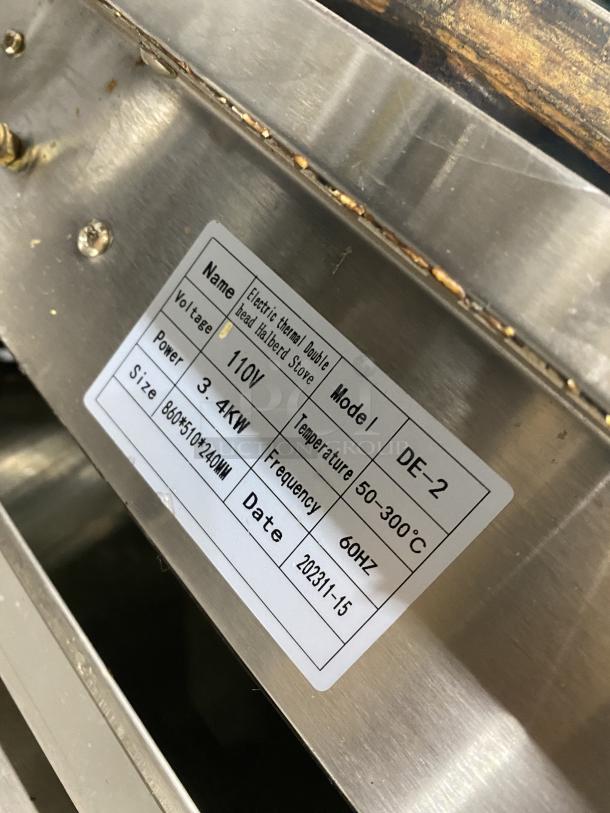 Commercial stainless steel electric double crepe maker, model DE-2, 110V, with label displaying specs and production date.