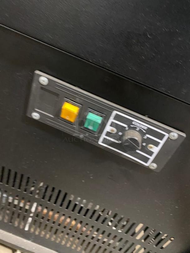 Black commercial refrigerated display case with slanted glass, wood-slatted base, sliding doors, rear prep area, and storage.