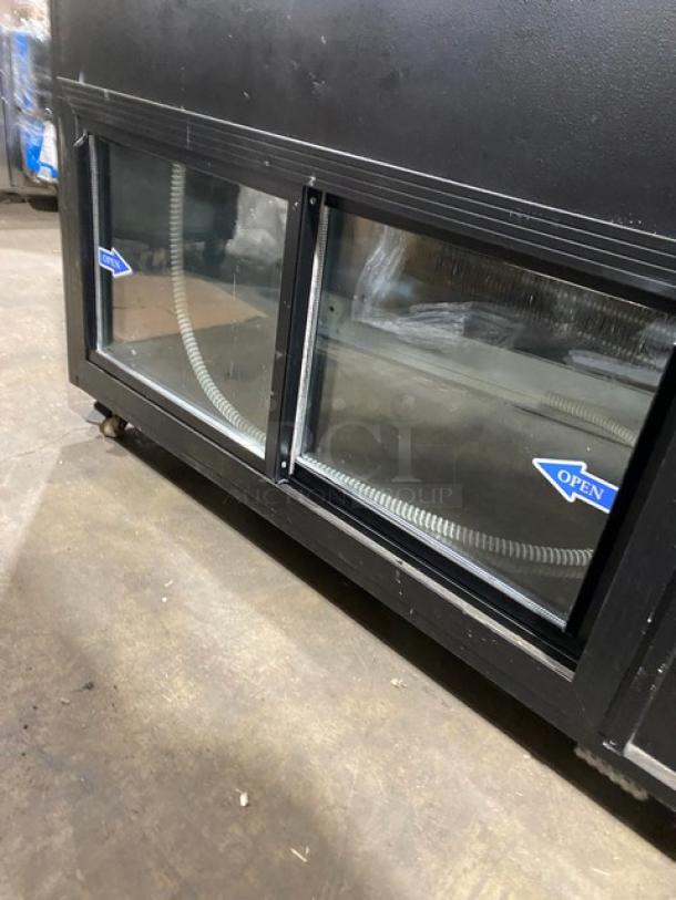 Commercial 60" black slanted glass deli display case with wood-slatted base, sliding doors, rear prep area, and storage on casters.