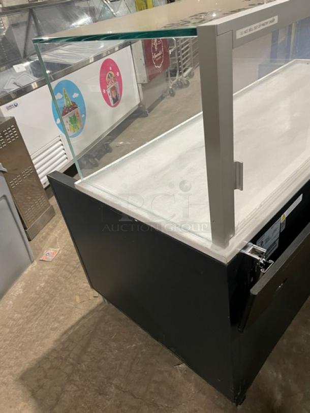 Structural Concepts SBZ6652DR black refrigerated grab-n-go display case with glass top, rear sliding doors, on legs.