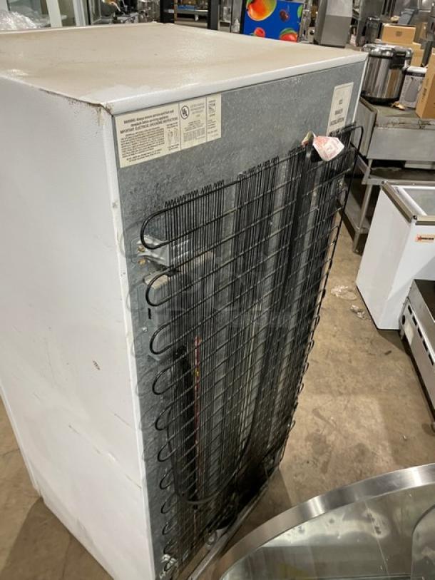 Frigidaire Commercial white top-freezer/refrigerator, model MRT18DNEW0. Features poly-coated wire racks, pull-out drawers. Visible labels detail electrical info.