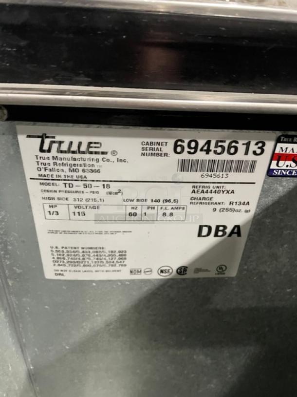 True TD-50-18 bottle cooler, black, 50" wide, stainless steel worktop, dual slide lids, 115V, SN: 6945613, made in USA.