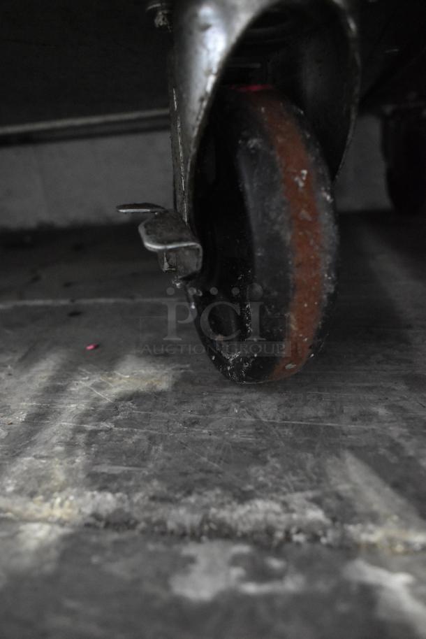 Close-up of a worn caster wheel on a Dukers commercial prep table, showing signs of use.