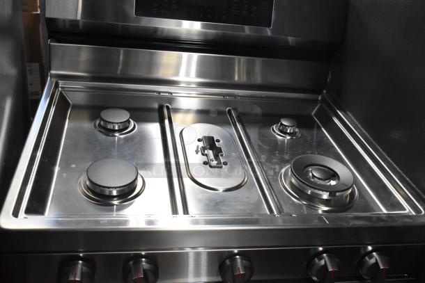 Gas-powered 4 burner range with 2 ovens. Stainless steel, missing grates, control knobs visible below burners.