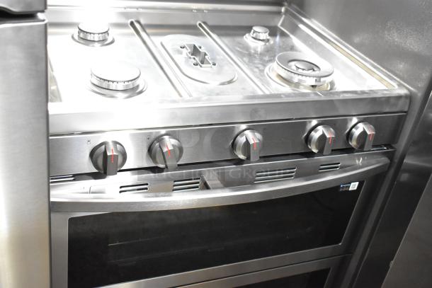 Gas-powered 4 burner range with 2 ovens, stainless steel. Missing grates. Features control knobs and oven window.
