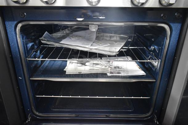 Gas-powered 4-burner range with 2 ovens, missing grates. Interior shows accessories and manuals. Good condition.