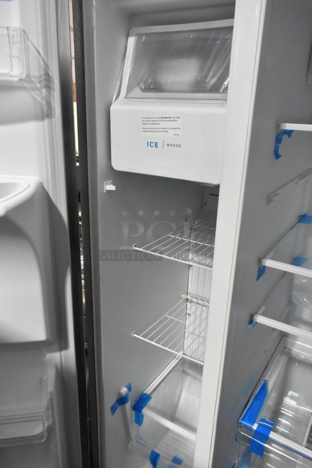 Alt Text: Brand new 2025 Frigidaire FRSS2623ASM cooler and freezer, showing interior ice maker, wire shelves, and protective tape.