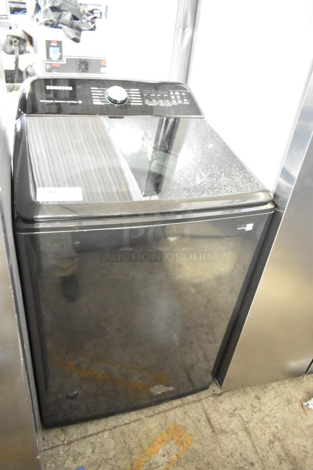 Samsung top load washer in black, features a digital control panel. Condition appears gently used. Model info not specified.