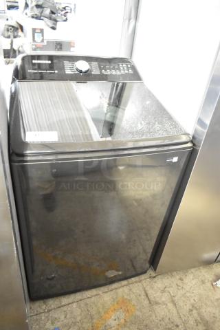 Samsung top load washer in black, features a digital control panel. Condition appears gently used. Model info not specified.